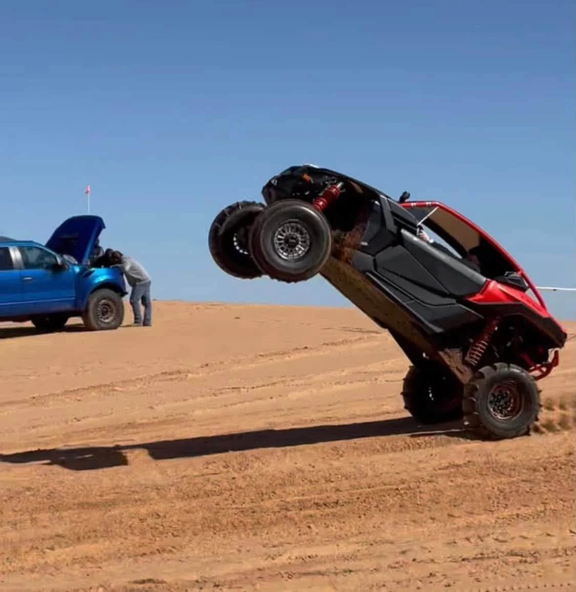 Red off-road side-by-side lifting its front wheels in sand dunes
