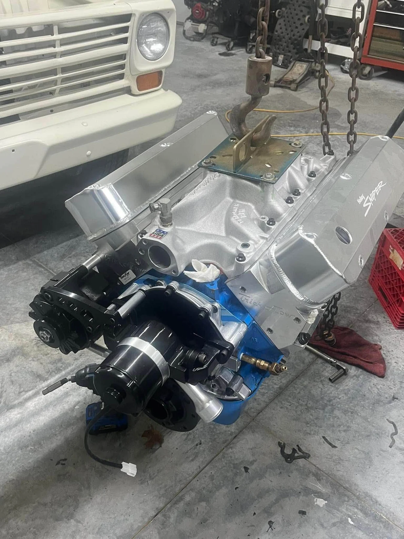 Engine assembly on a hoist in front of a classic truck