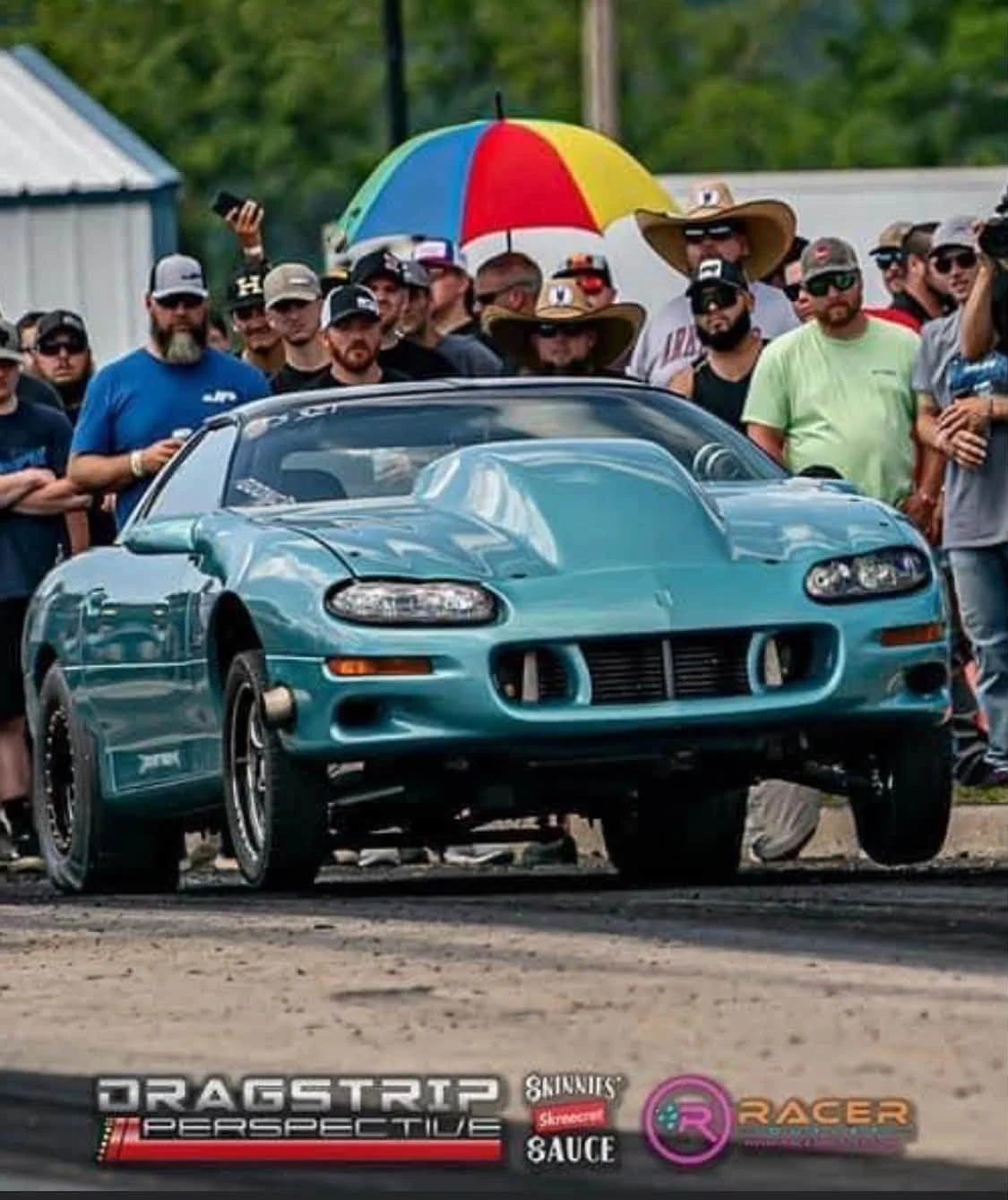 Turquoise Camaro at a drag racing event surrounded by enthusiasts
